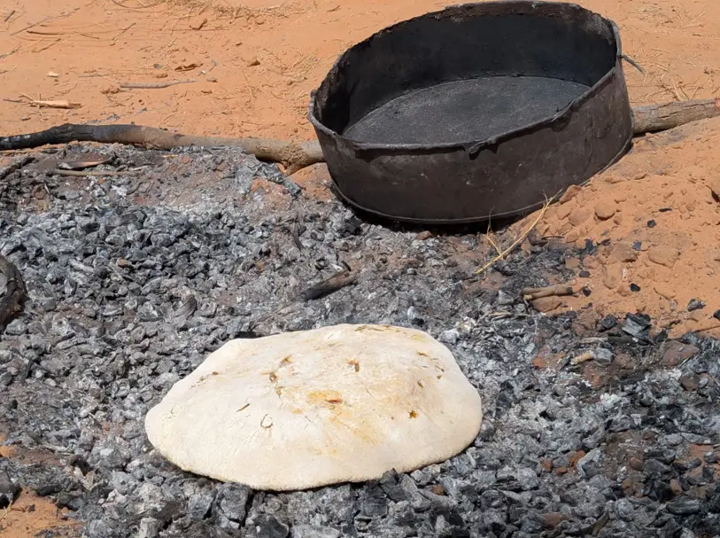 Masa de medfouna cociéndose sobre arena caliente y brasas en el desierto de Marruecos